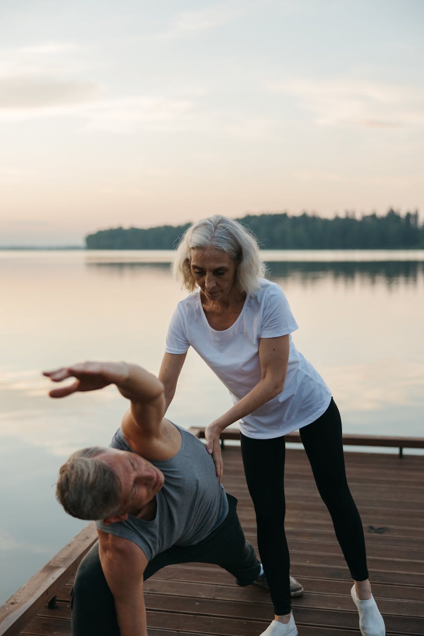 Woman practicing yoga on a wooden dock by a serene lake at sunrise.